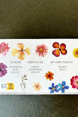 Back side of gift box with various colored flowers against white background and black lettering detailing ingredients such as rose, sunflower and jasmin on black table