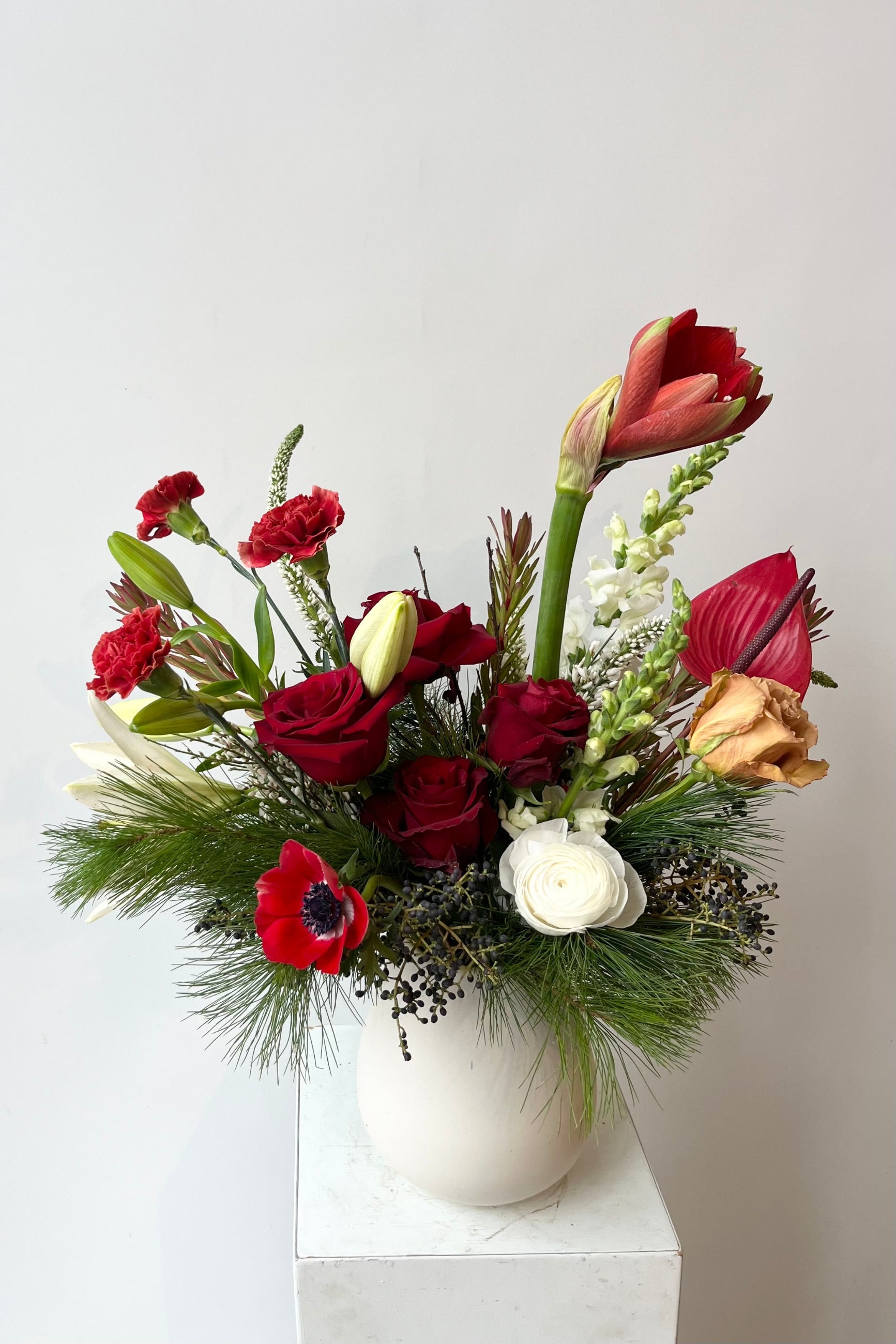 A hand holds an example of fresh Floral Arrangement Solstice with asparagus fern greens and reds from Sprout Home Floral in Chicago #size_$160