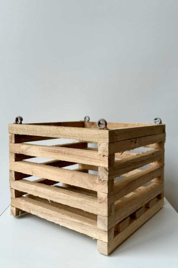 Side view of a wooden slatted vanda basket with metal rings for string attachment, not included, against white background