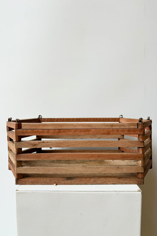 Side view of elongated wooden hexagonal slatted basket with metal rings for string attachment, not included, against white background. 