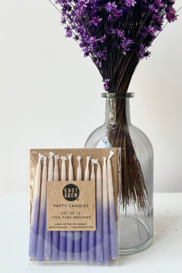 Set of twelve short, ombre violet beeswax candles in cellophane wrap against white background 