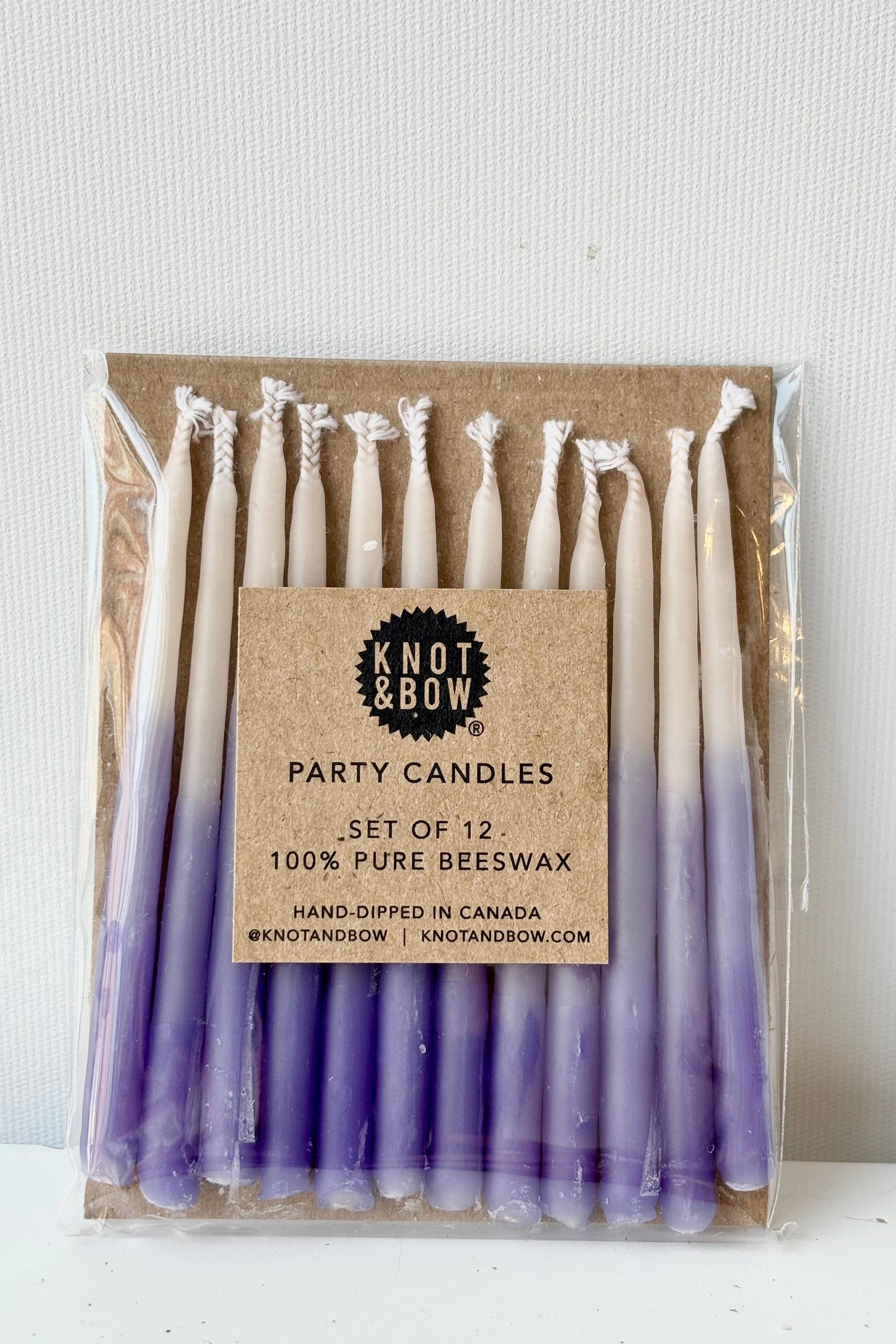 Set of twelve short, ombre violet beeswax candles in cellophane wrap against white background 