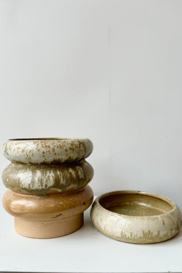 Ribbed stoneware planter with detachable saucer featuring various glazes in white, olive, gold and peach throughout against white background