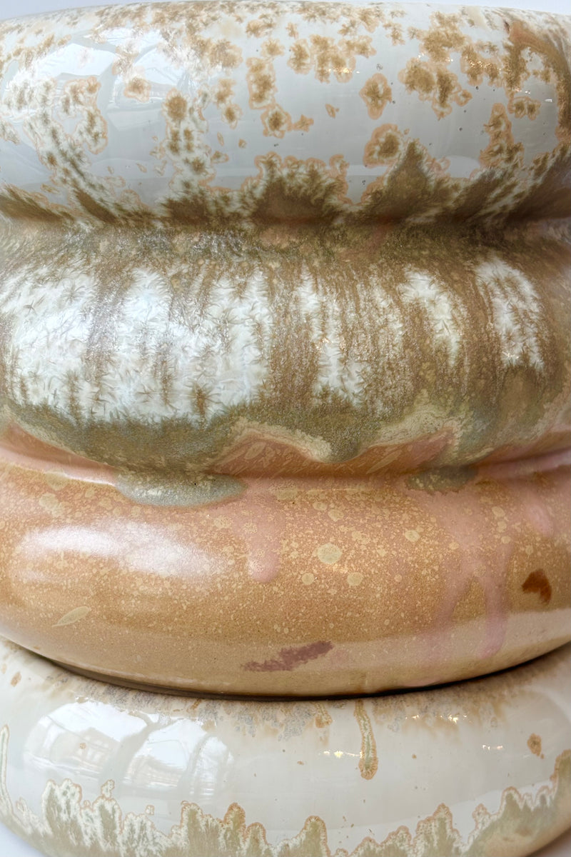 Close up of ribbed stoneware planter featuring various glazes in white, olive, gold and peach throughout against wihte background