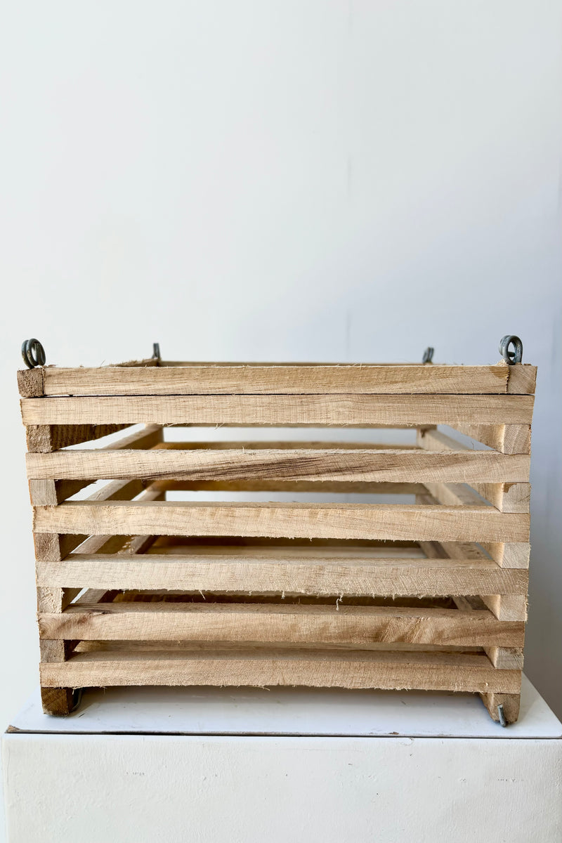 Side view of a wooden slatted vanda basket with metal rings for string attachment, not included, against white background