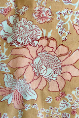 Close up of hand block printed Panjim tablecloth with a gold and pink floral motif with maroon accents against white background.