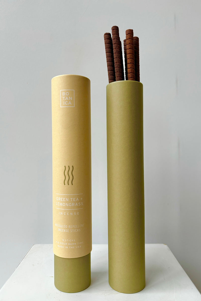 Two kraft paper and green colored cardboard tubes showing front of packaging and interior with green tea and lemon grass incense sticks against white wall