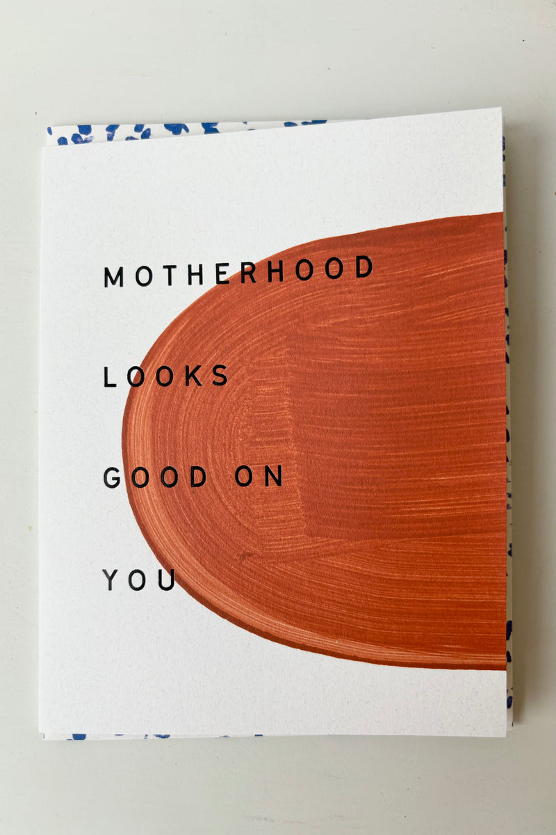 Painted greeting card with brown abstract design against white background with blue lettering that says motherhood looks good on you