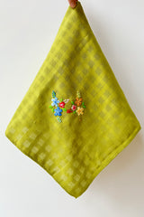 Green handmade tea towel with embriodered floral motif against white background