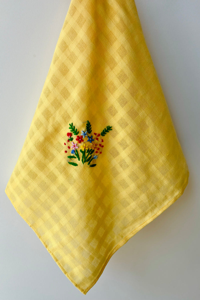 Yellow handmade tea towel with embriodered floral motif against white background