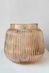 Rose color tinted, wide mouth glass vase with vertical ribbing against white background