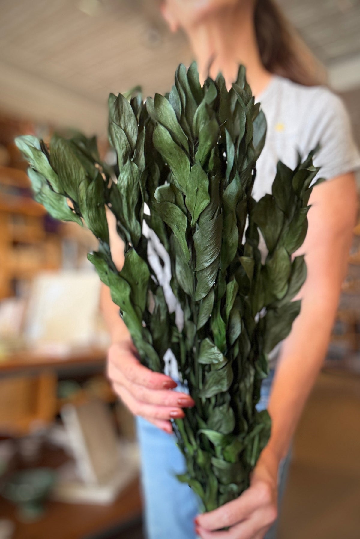 person holding a Ruscus Gigante Natural Green Colored Preserved Bunch at Sprout Home Floral ©Sprout Home