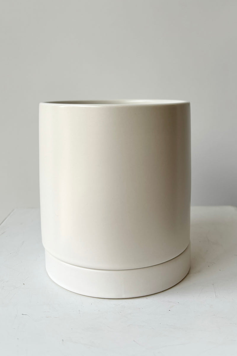 Ceramic, white glazed cylinder planter with drainage hole and tray against grey background