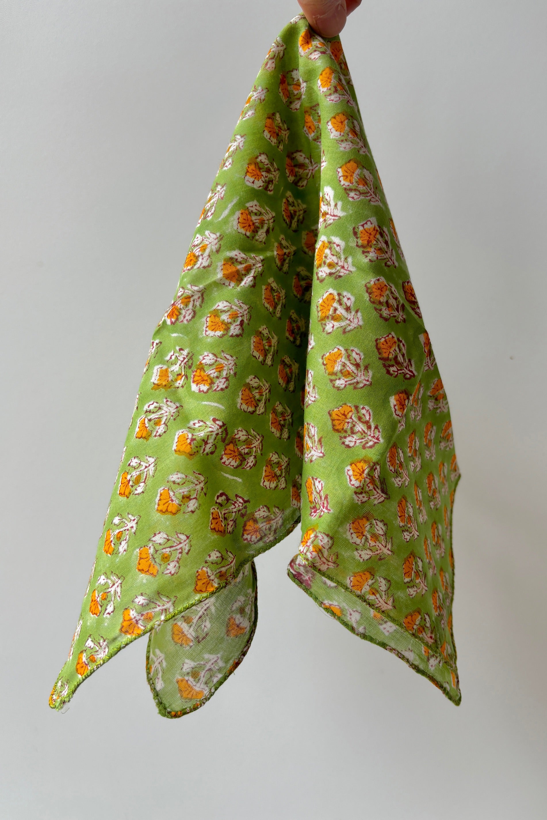 Hand sewn cloth napkin with orange flowers on green background against white wall