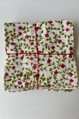 Set of four white hand sewn napkins with small pink flowers on leafy green vines patterned throughout on a white background