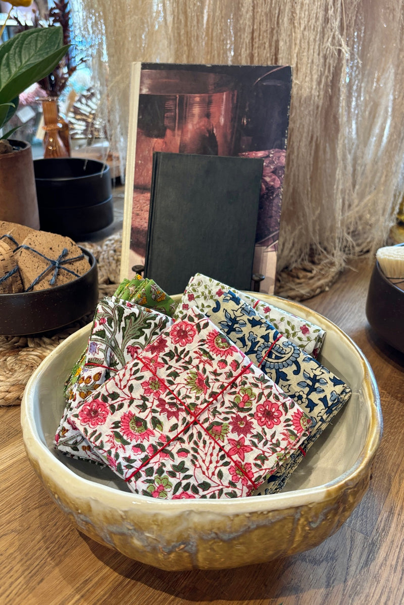 Assorted sets of hand sewn napkins displayed in a ceramic bowl on a wooden table