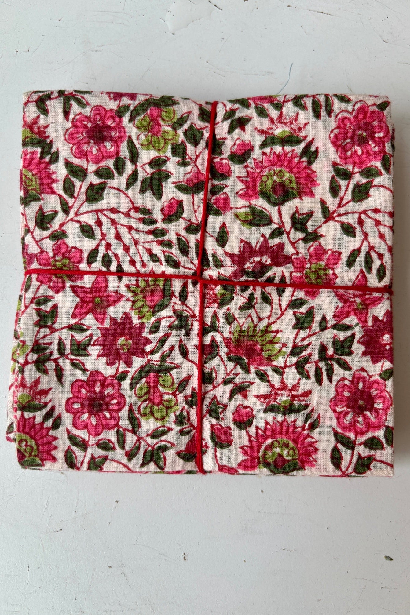 Set of four hand sewn napkin with pink and green flower print throughout on light pink background on white table