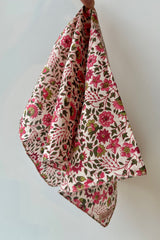 Hand sewn napkin with pink and green flower print throughout on light pink background against a white wall