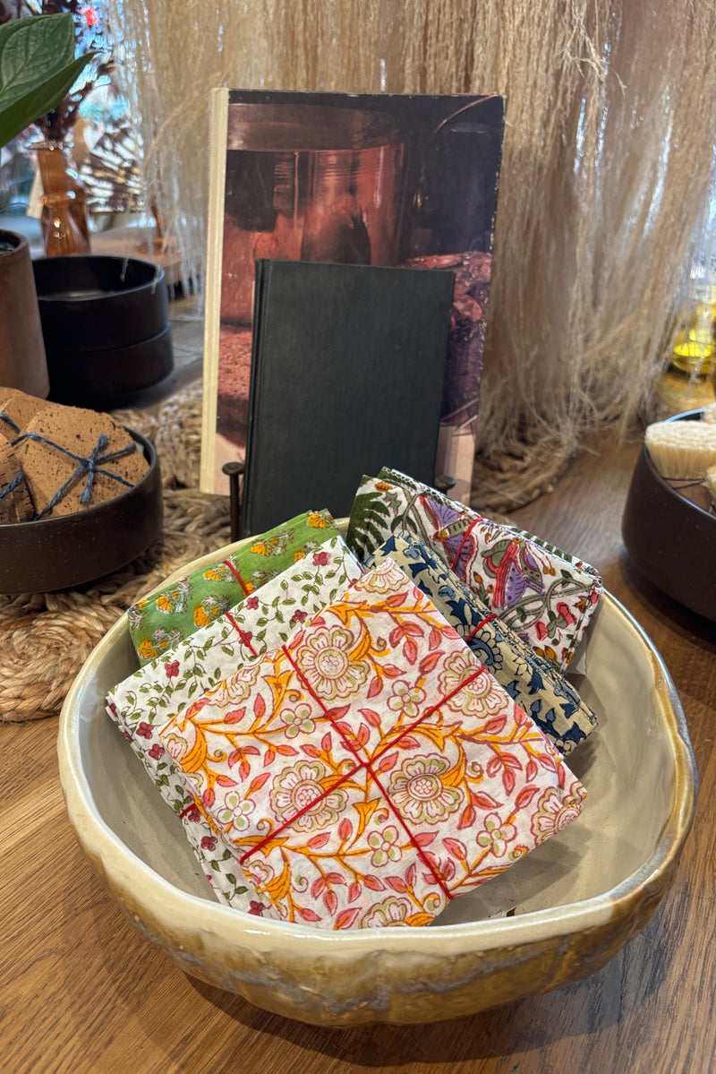 Assorted sets of hand sewn fabric napkins displayed in a ceramic bowl on a wooden table