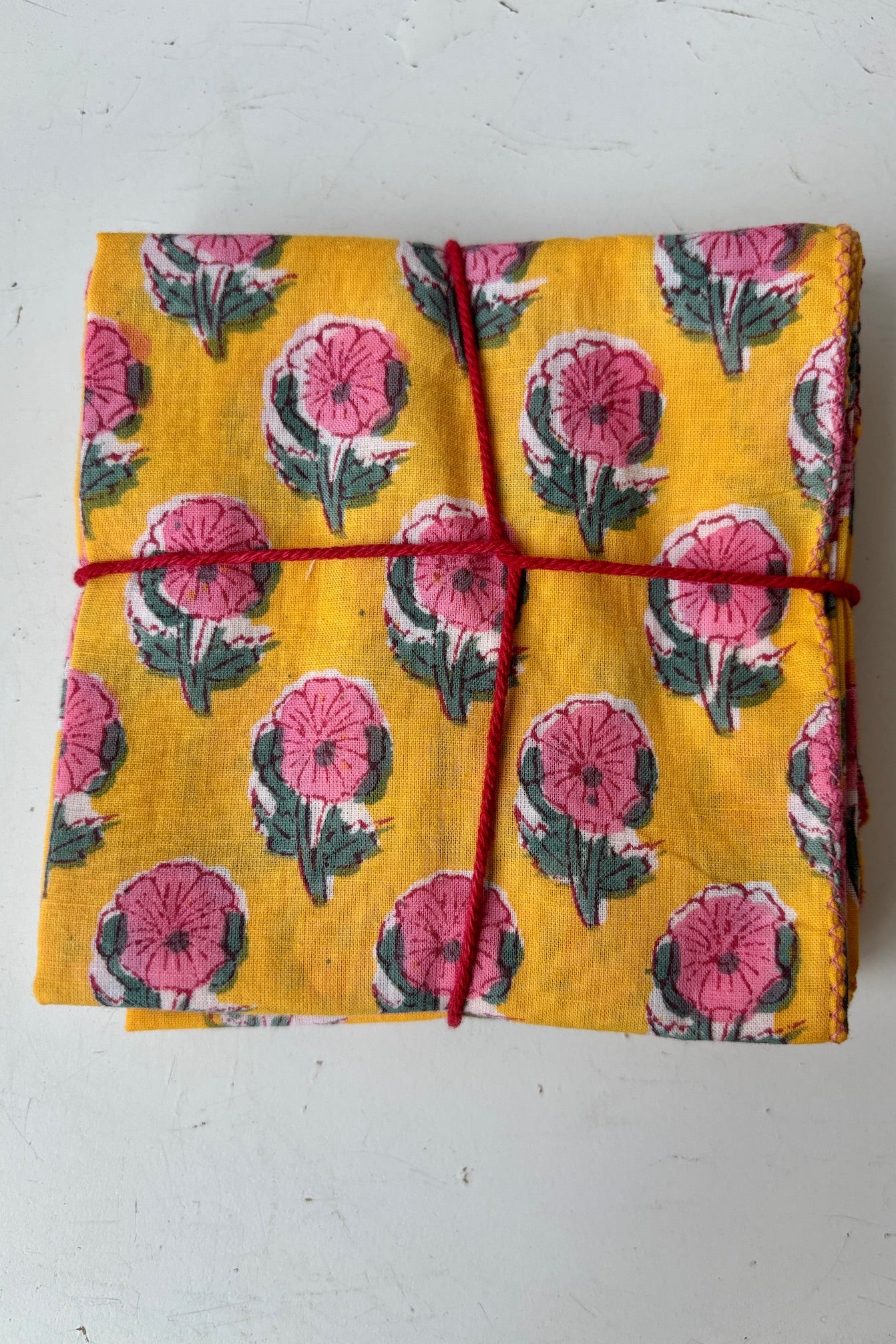 Set of four handsewn napkins with pink and green flowers on a golden yellow background against white background