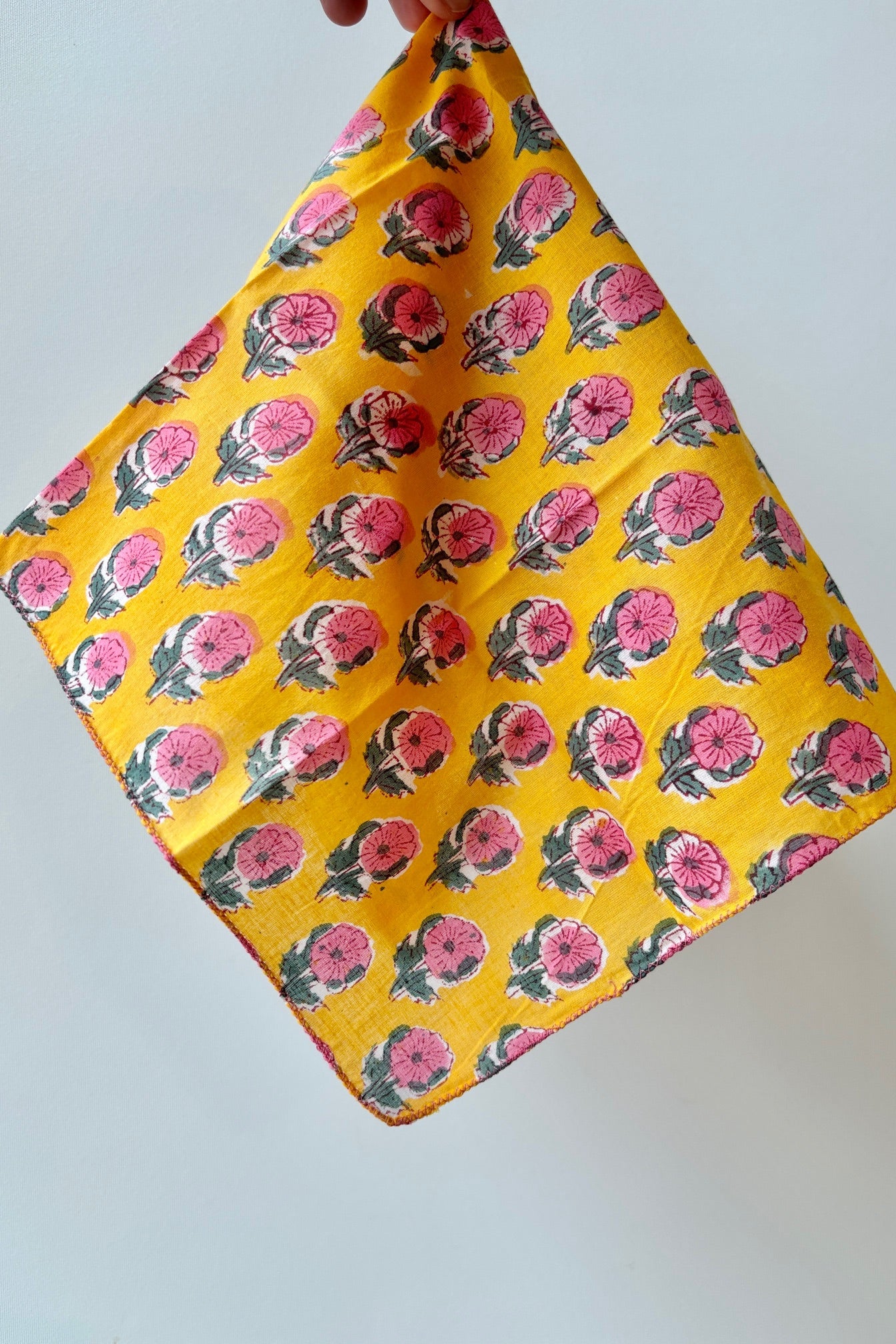 Handsewn napkin with pink and green flowers on a golden yellow background against white background