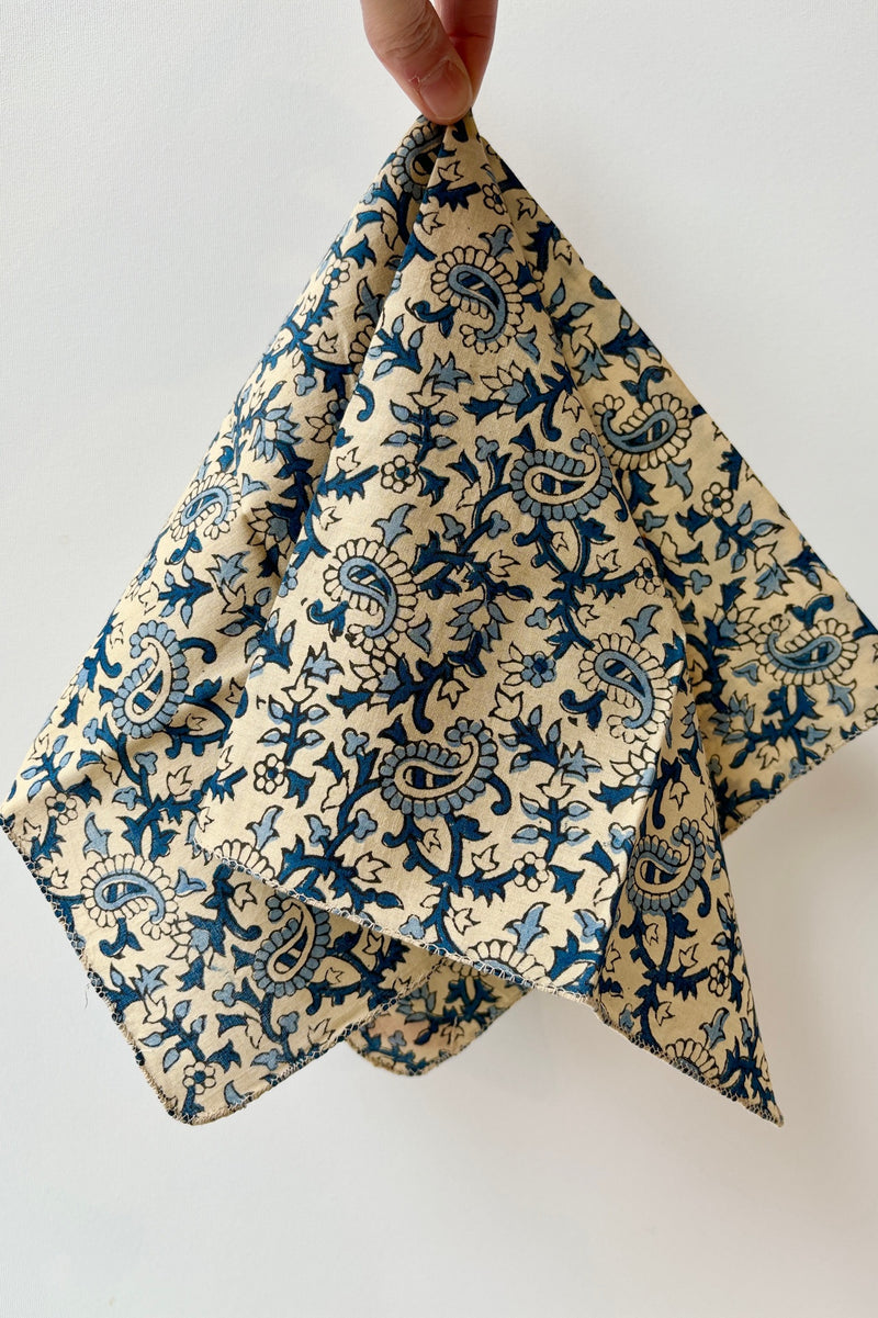 Handsewn napkin with dark and light blue filagree design throughout over cream colored background 