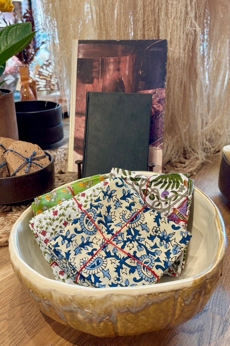 Assorted sets of hand sewn fabric napkins displayed in a ceramic bowl on a wooden table