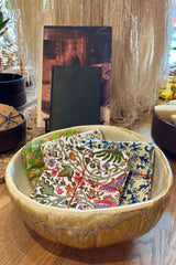 Assorted sets of hand sewn fabric napkins displayed in a ceramic bowl on a wooden table