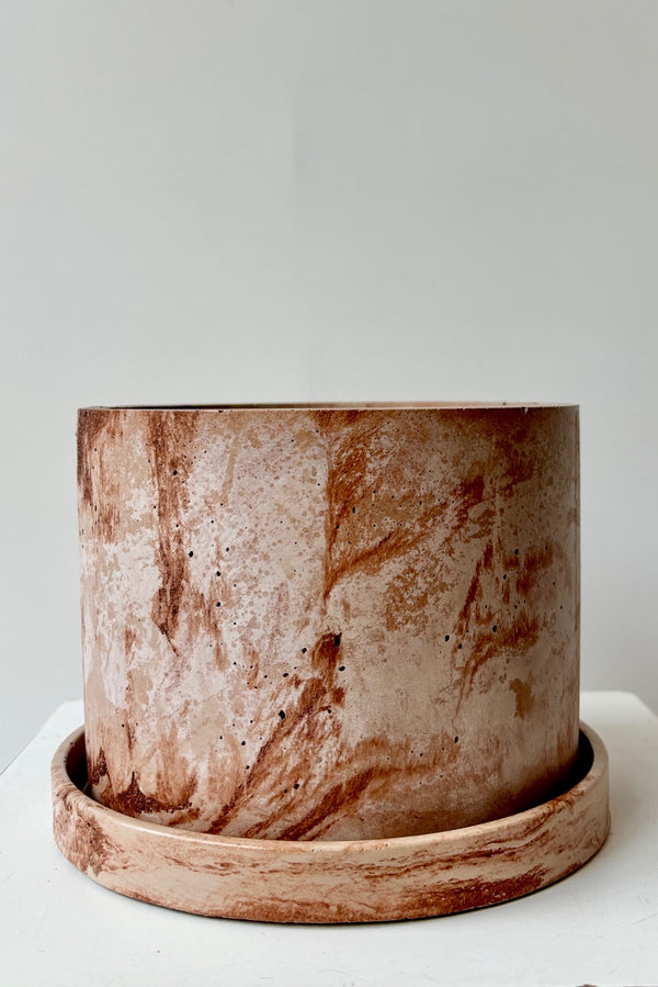 Marbled brown and white varnished cement planter with drain hole and saucer against a white wall