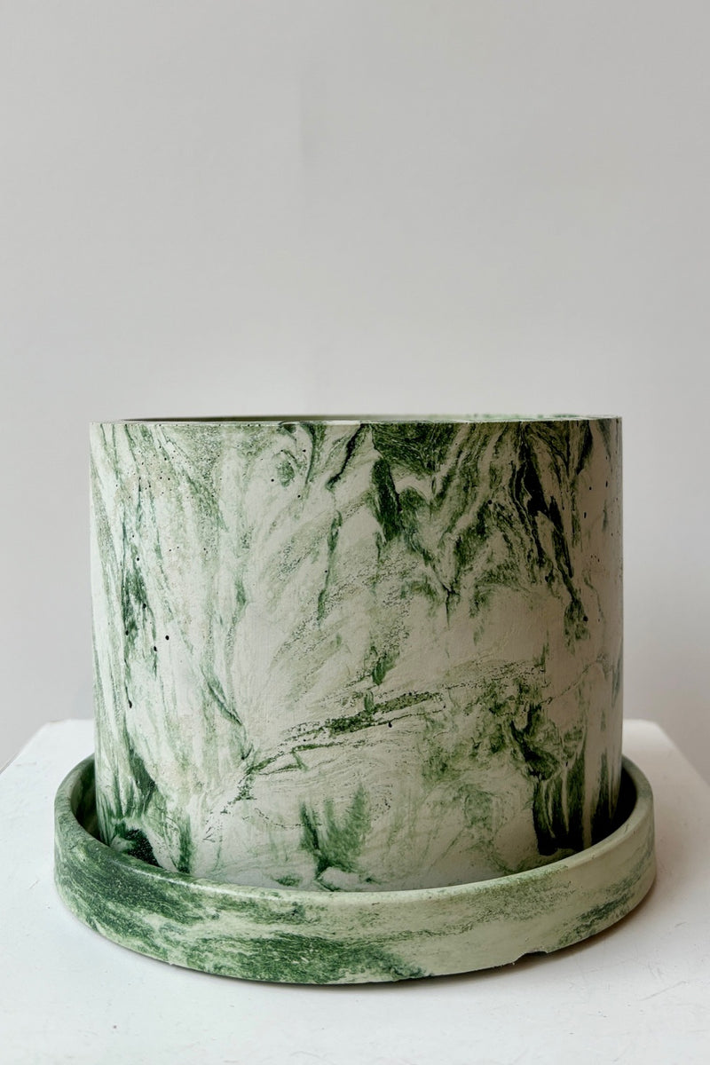 Marbled green and white varnished cement planter with drain hole and saucer against a white wall