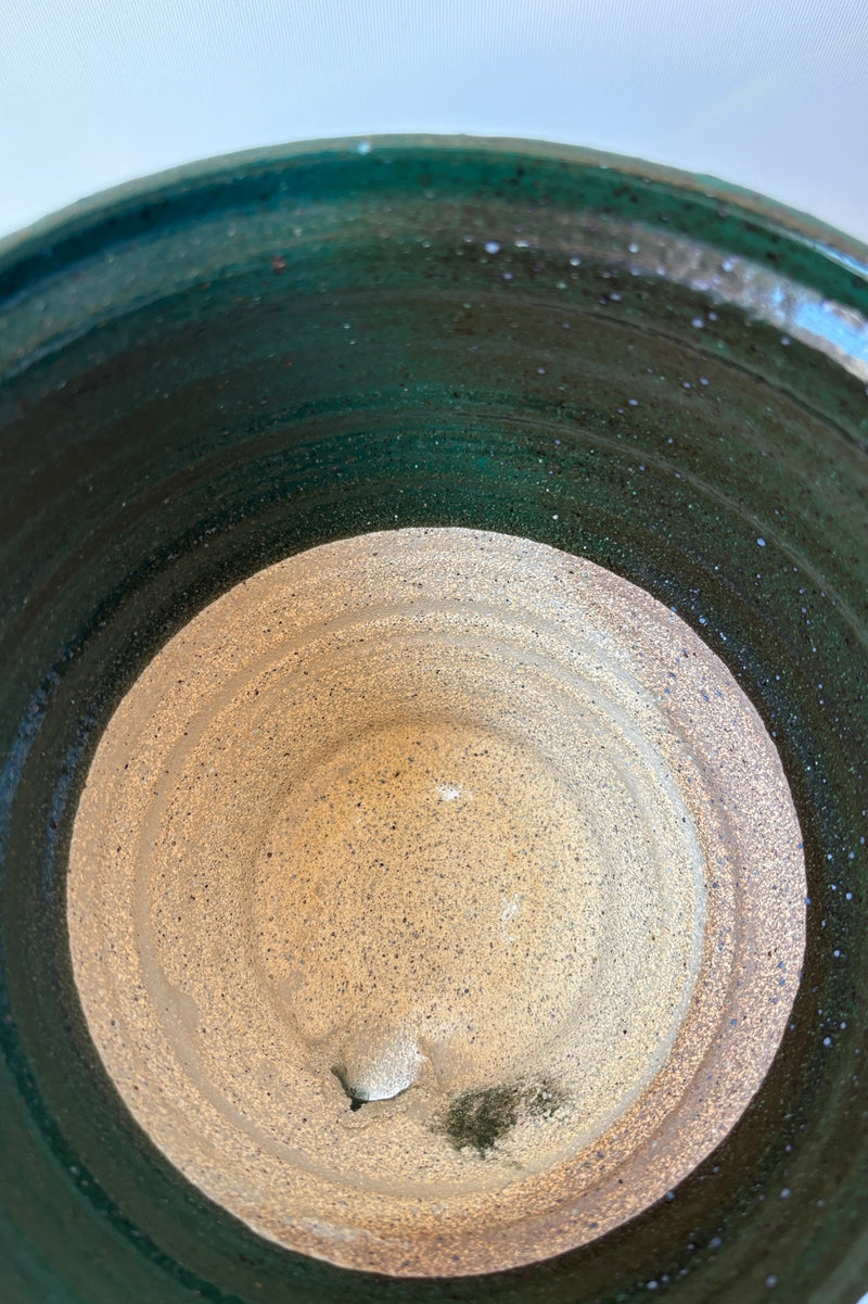 Interior of clay planter with jade green glaze over top half of planter and bare clay on bottom half with drainage hole and attached tray