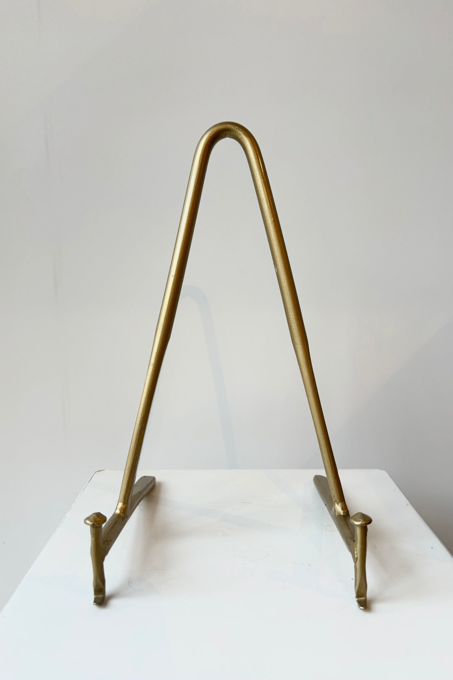 Brass display stand featuring two horizontal prongs connected by a vertical arch for support against a white background ©Sprout Home