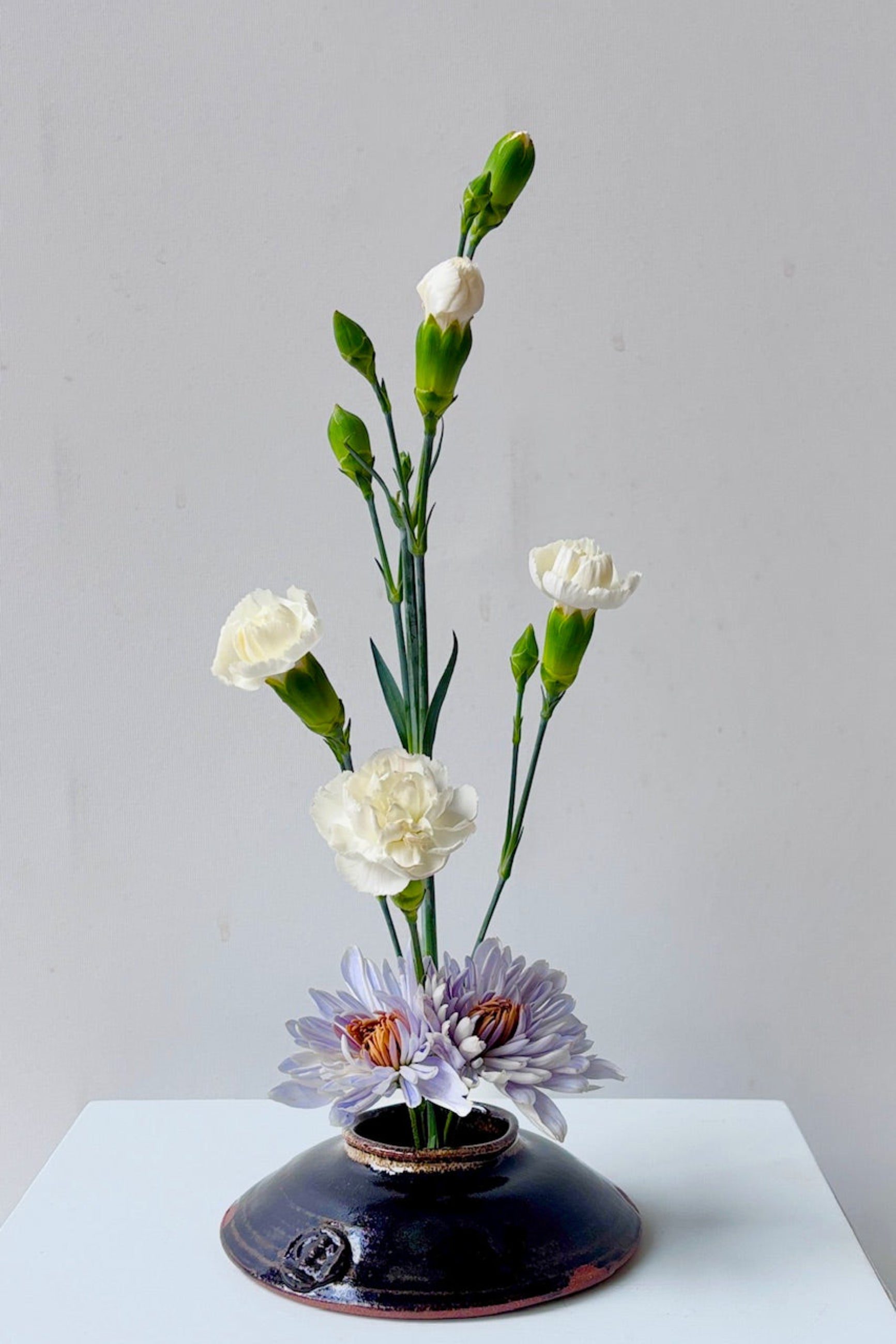 Glazed black ceramic Ikebana vase with flowers against a white background ©Sprout Home