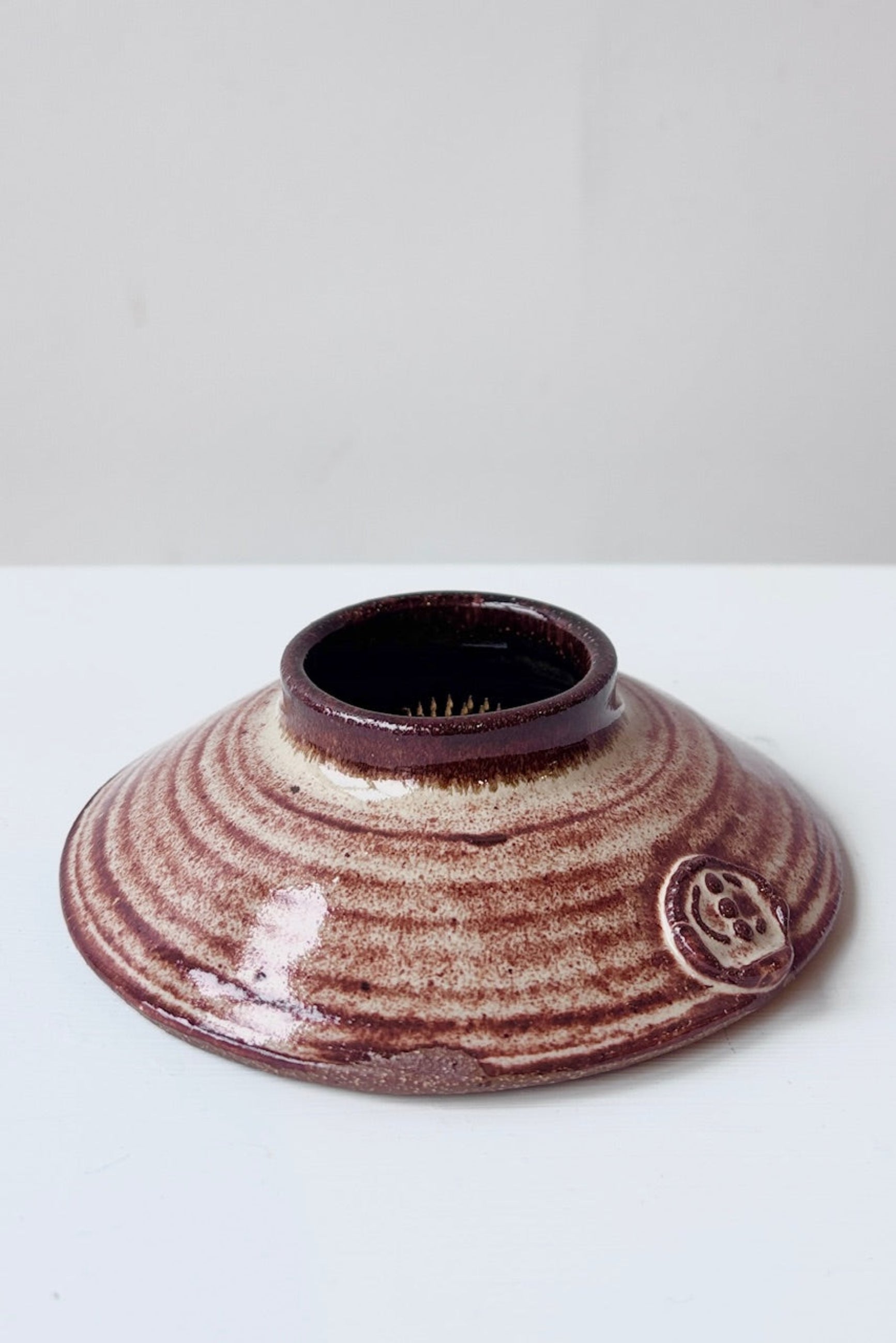 Rust and cream colored, round, low Ikebana vase with attached floral frog against a white surface ©Sprout Home