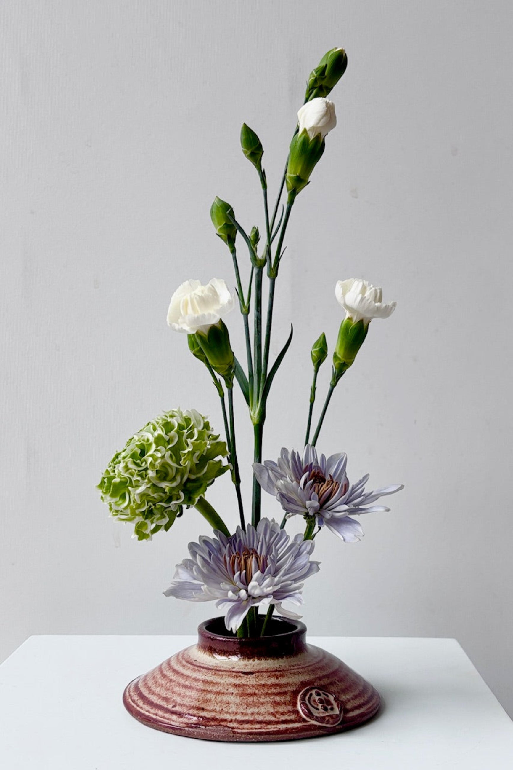 Rust and cream colored Ikebana vase with flowers against a grey background ©Sprout Home
