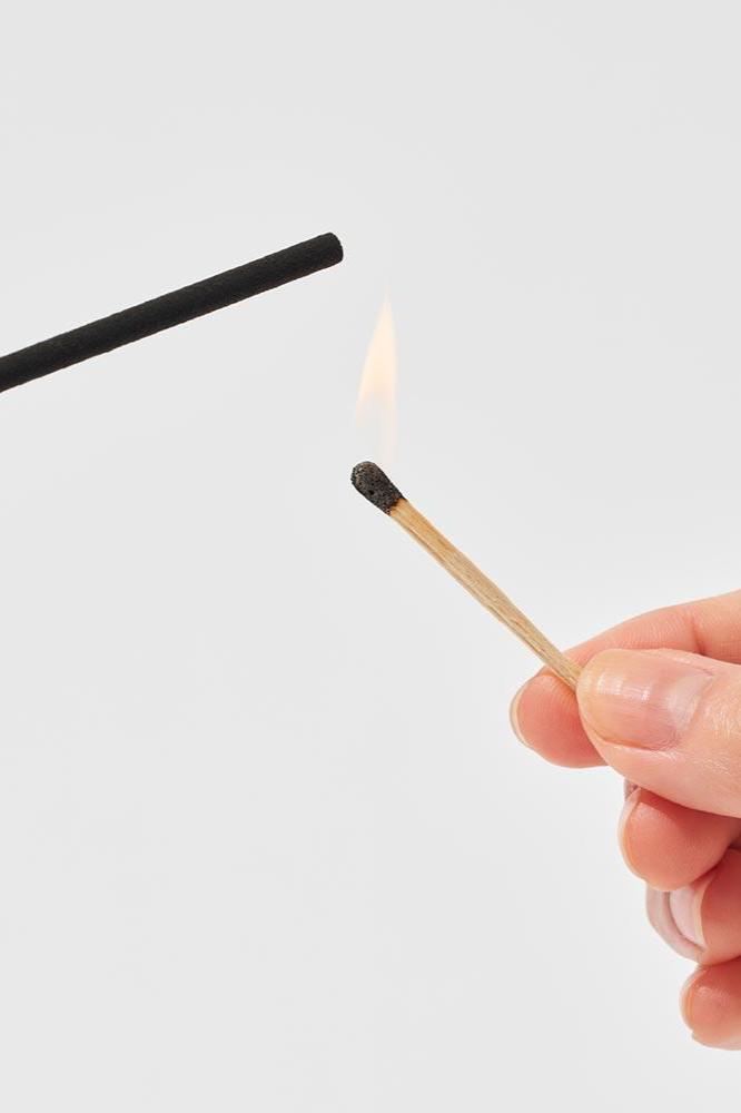 Lighting an Elements incense stick with a match detail.