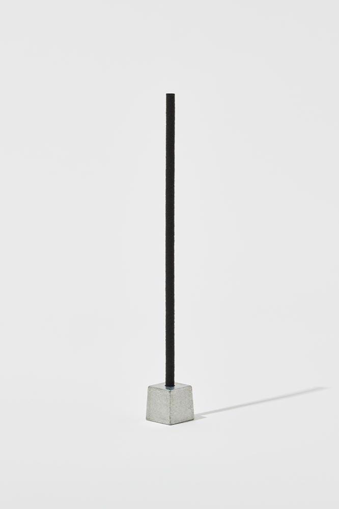 An Elemense incense stick in its metal holder against a white background.