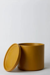 Solid Goods Cylinder and saucer in Mustard shown with its saucer leaning against the pot by LBE Design