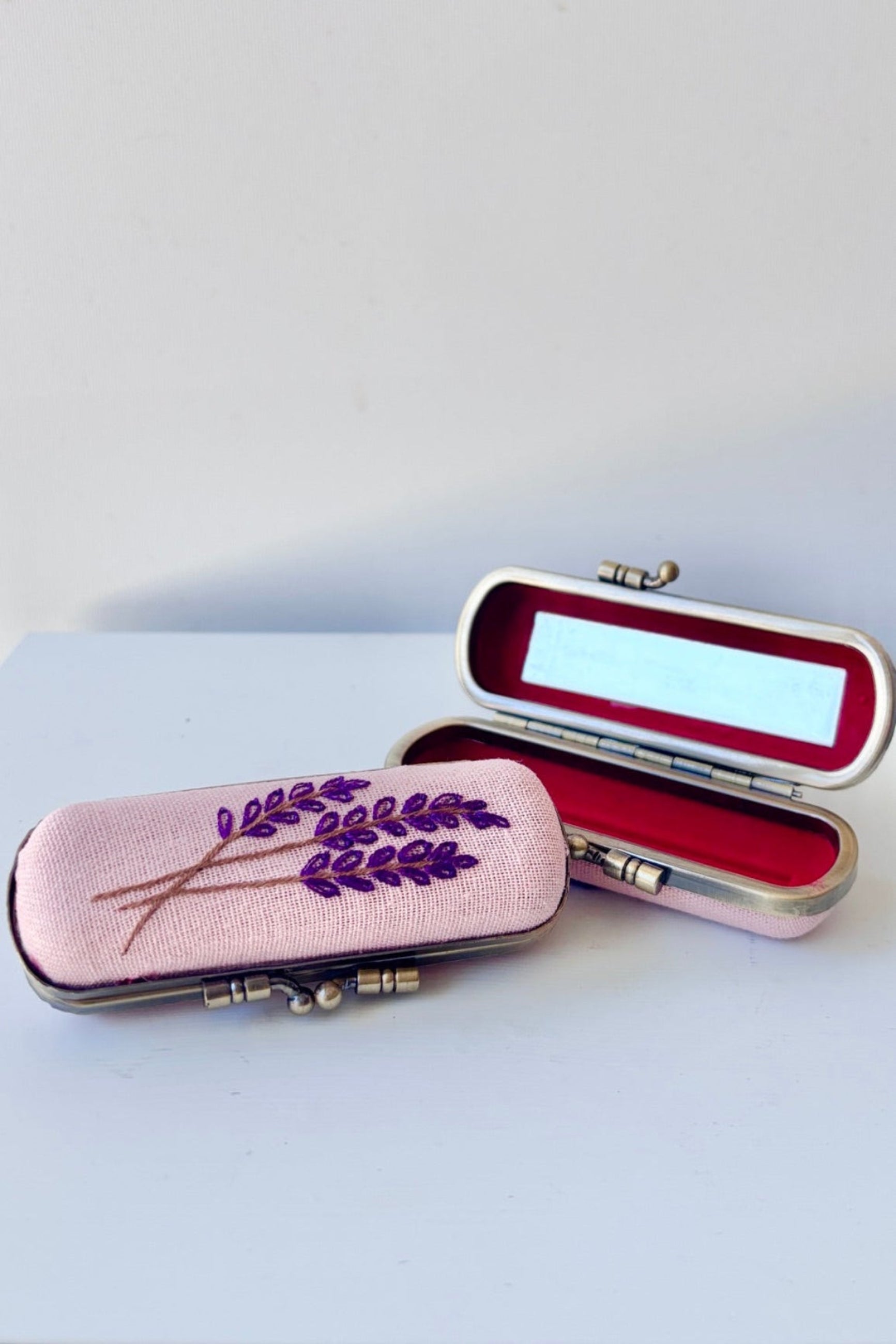 Decorative case with floral embroidery on a lavender background with red velvet and  mirror inside ©Sprout Home