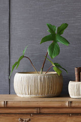 The large concrete faux rattan planter with a plant inside and sitting on a wood dresser.