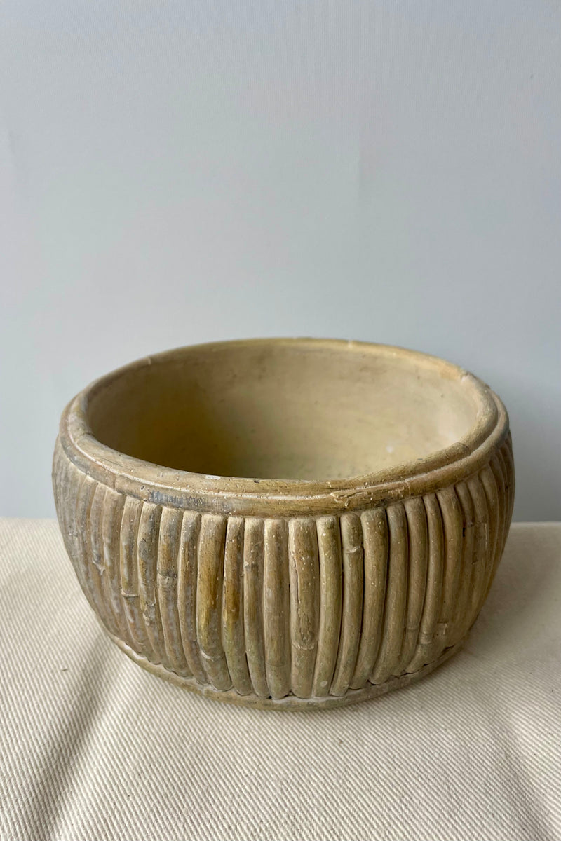 Large shallow concrete faux rattan planter empty against a white background on a white tablecloth looking slightly from above.