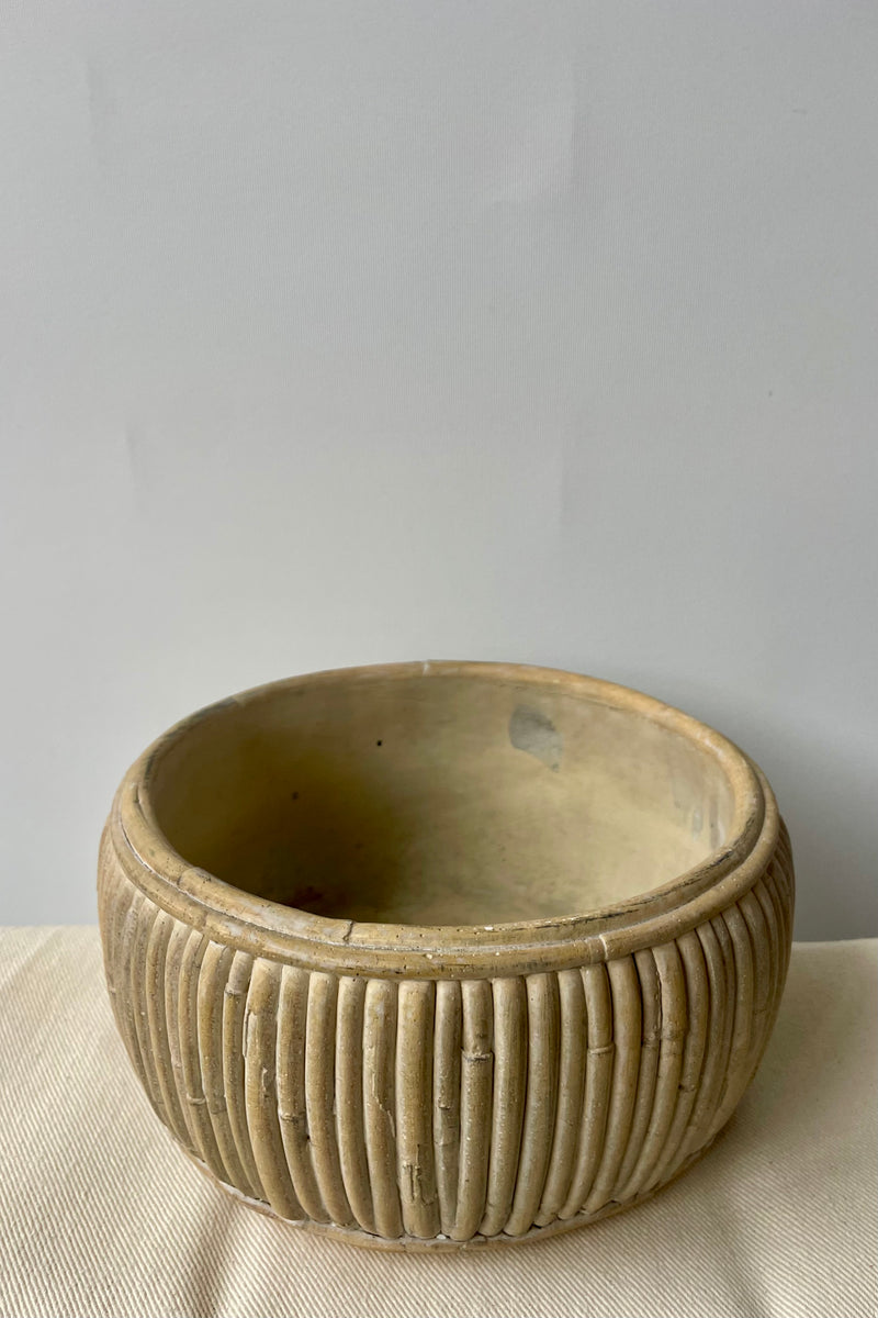 Small shallow concrete faux rattan planter empty against a white background on a white tablecloth looking slightly from above.