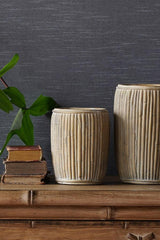 Small concrete tall faux rattan planter in the center with books to one side and a medium planter to the other on top of a wooden dresser.