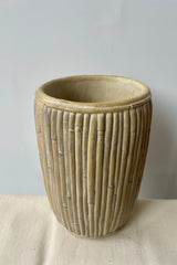 Large tall concrete faux rattan planter against a white background on a white tablecloth shown slightly from above.