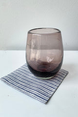 The Erin linen coaster sitting on a white surface with a purple glass on top.