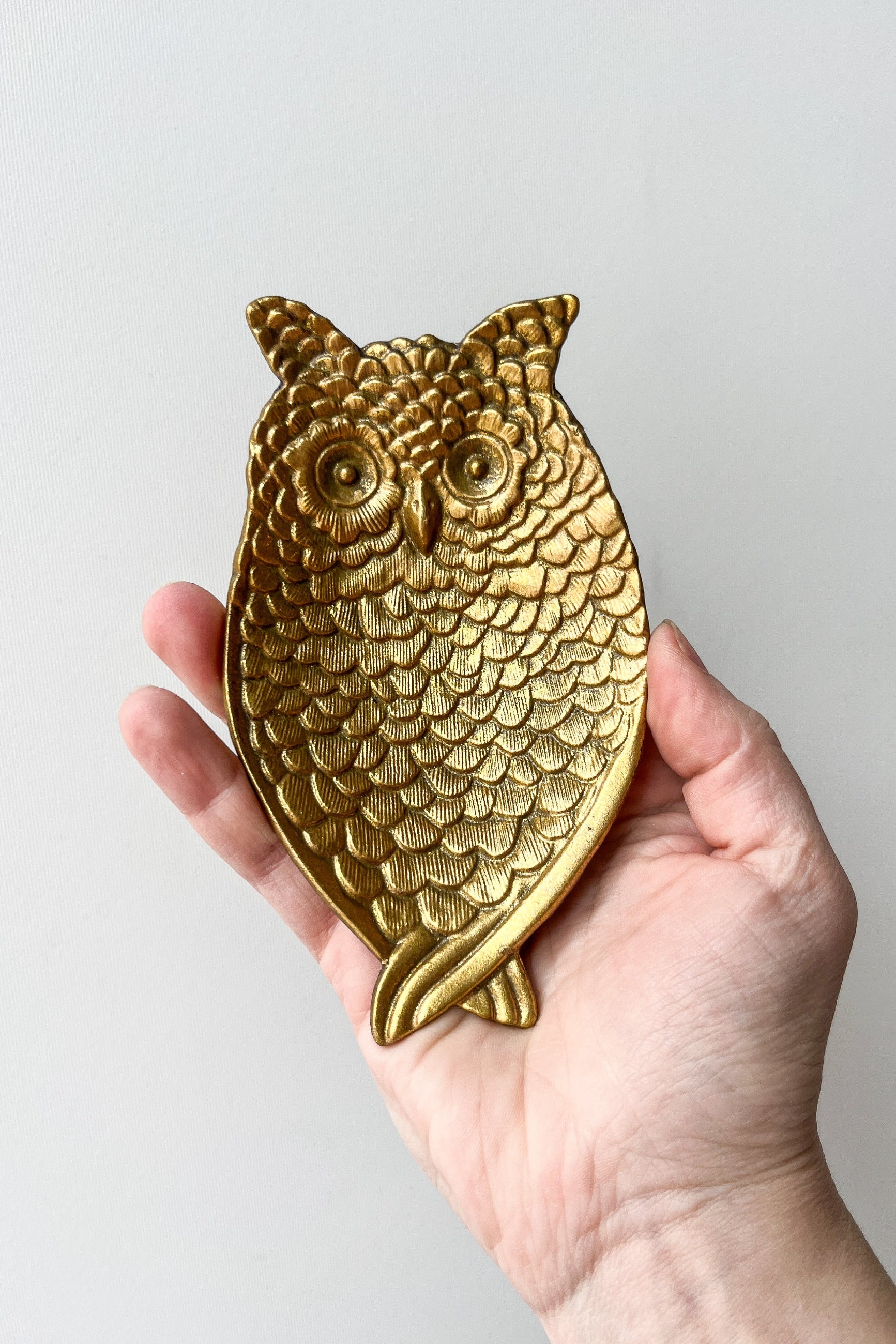 Gold owl-shaped object held in a hand against a light gray background ©Sprout Home