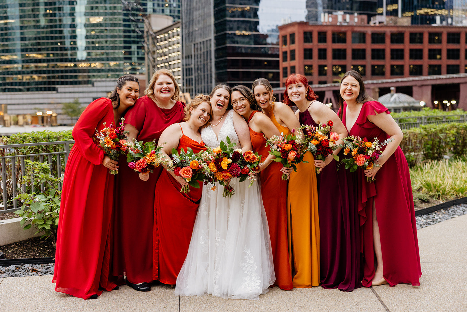 Bride and bridesmaids in red and warm toned dresses with floral bouquets by Sprout Home  in downtown Chicago ©Victoria Saint Marie Photography