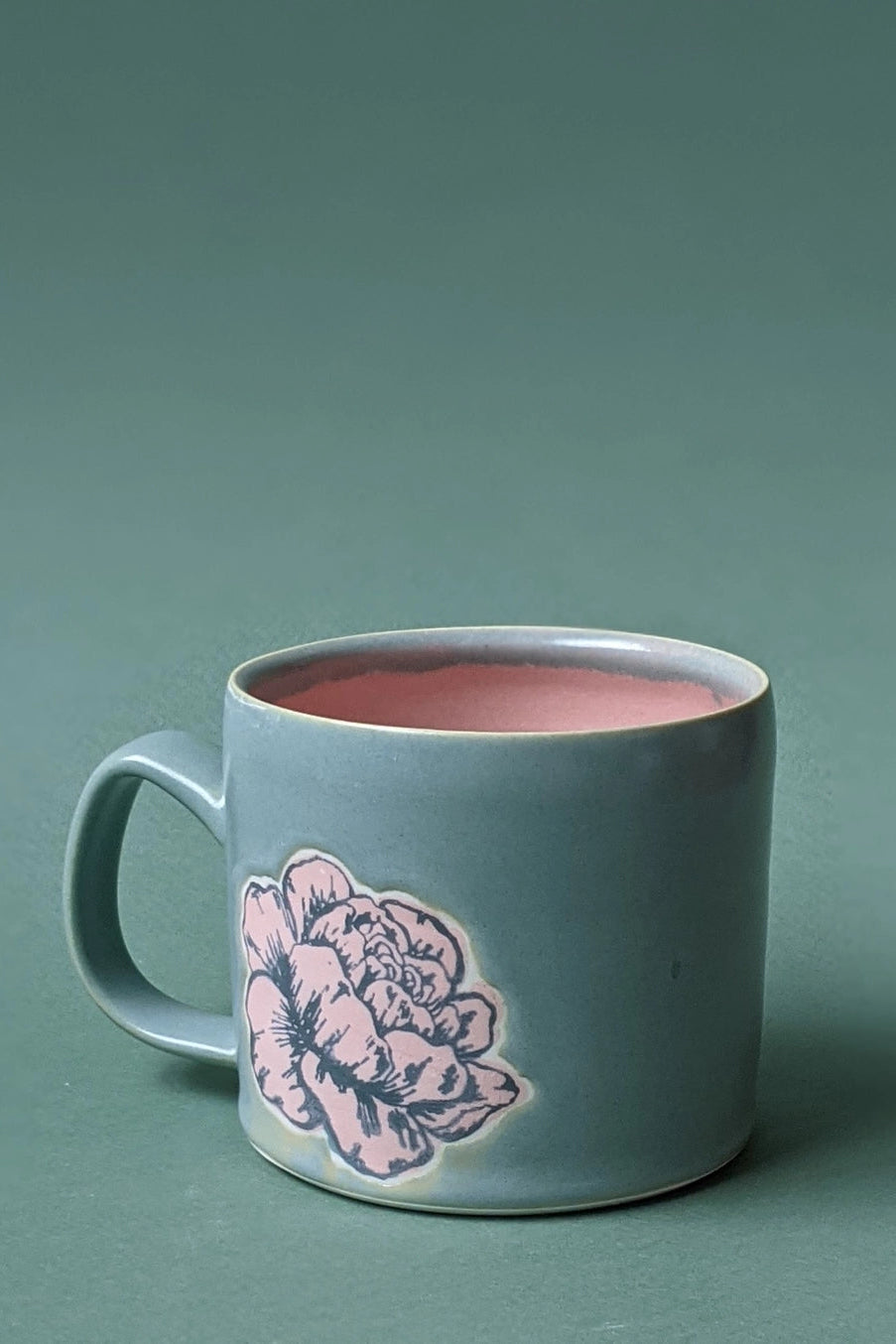 Teal mug with floral design filled with pink liquid on a teal background ©City in Bloom Ceramics