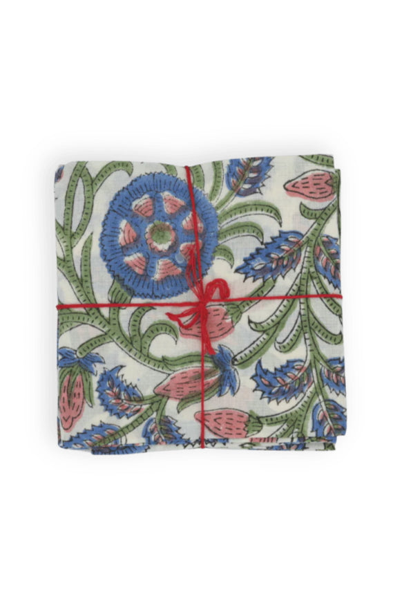 Photo of square folded napkins with a primarily blue floral pattern, tied with a red string on a white background ©Suzette a Table
