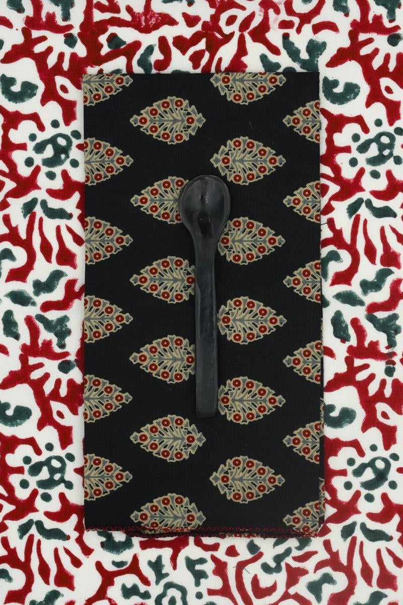 A black napkin with floral pattern set on a colorful tablecloth and displayed with a black spoon ©Sprout Home